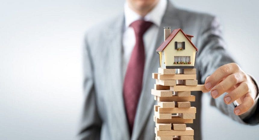 A man in a suit and tie standing behind a house on top of blocks.