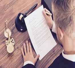 A man writing on paper next to a laptop.