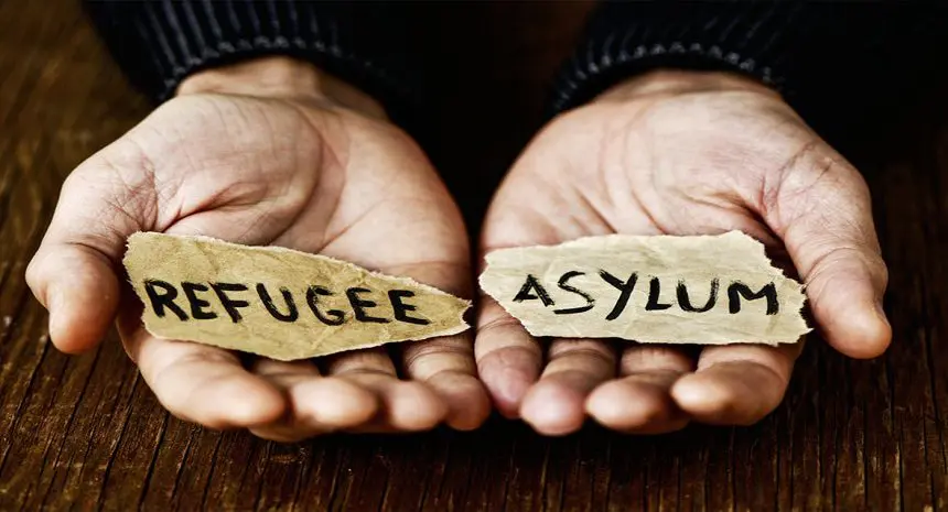 Two hands holding paper with refugees and asylum written on them.