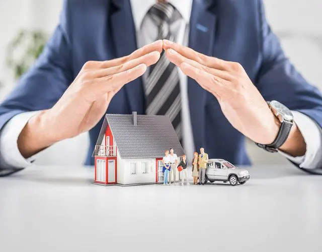 A man and woman are holding hands over a miniature house.